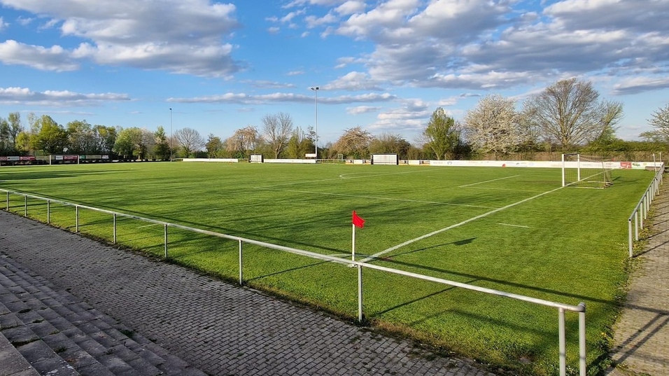 Weitl&auml;ufige Fu&szlig;ballplatzansicht mit gr&uuml;nem Rasen, Toren und Wolken am blauen Himmel.