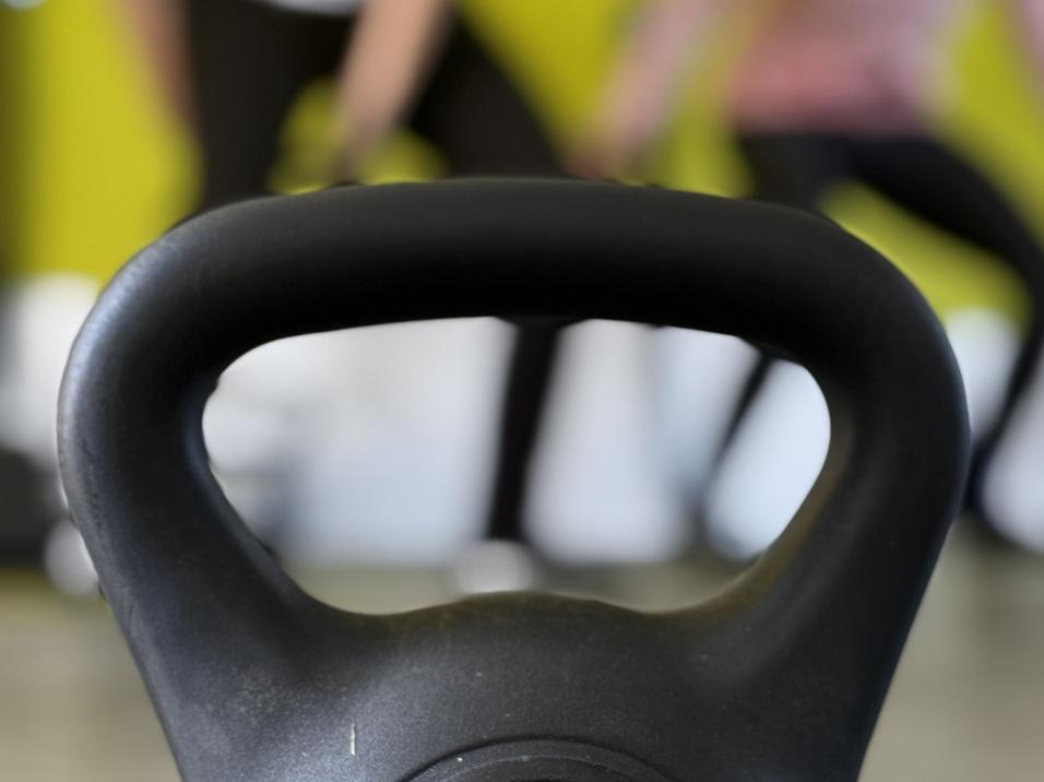 Schwarzfarbener Kettlebell mit der Beschriftung "Gorilla Sports 8 kg" im Vordergrund, unscharfe Personen beim Training im Hintergrund.