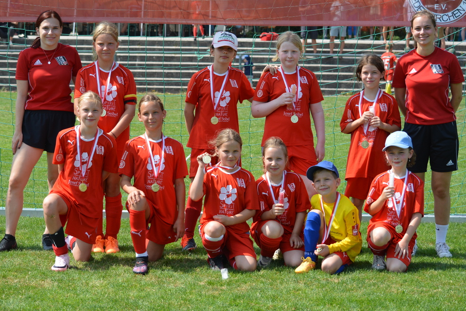 Mannschaft aus zw&ouml;lf M&auml;dchen in roten Trikots mit Medaillen vor einem Banner mit der Aufschrift &bdquo;Youngsters in Red&ldquo;.