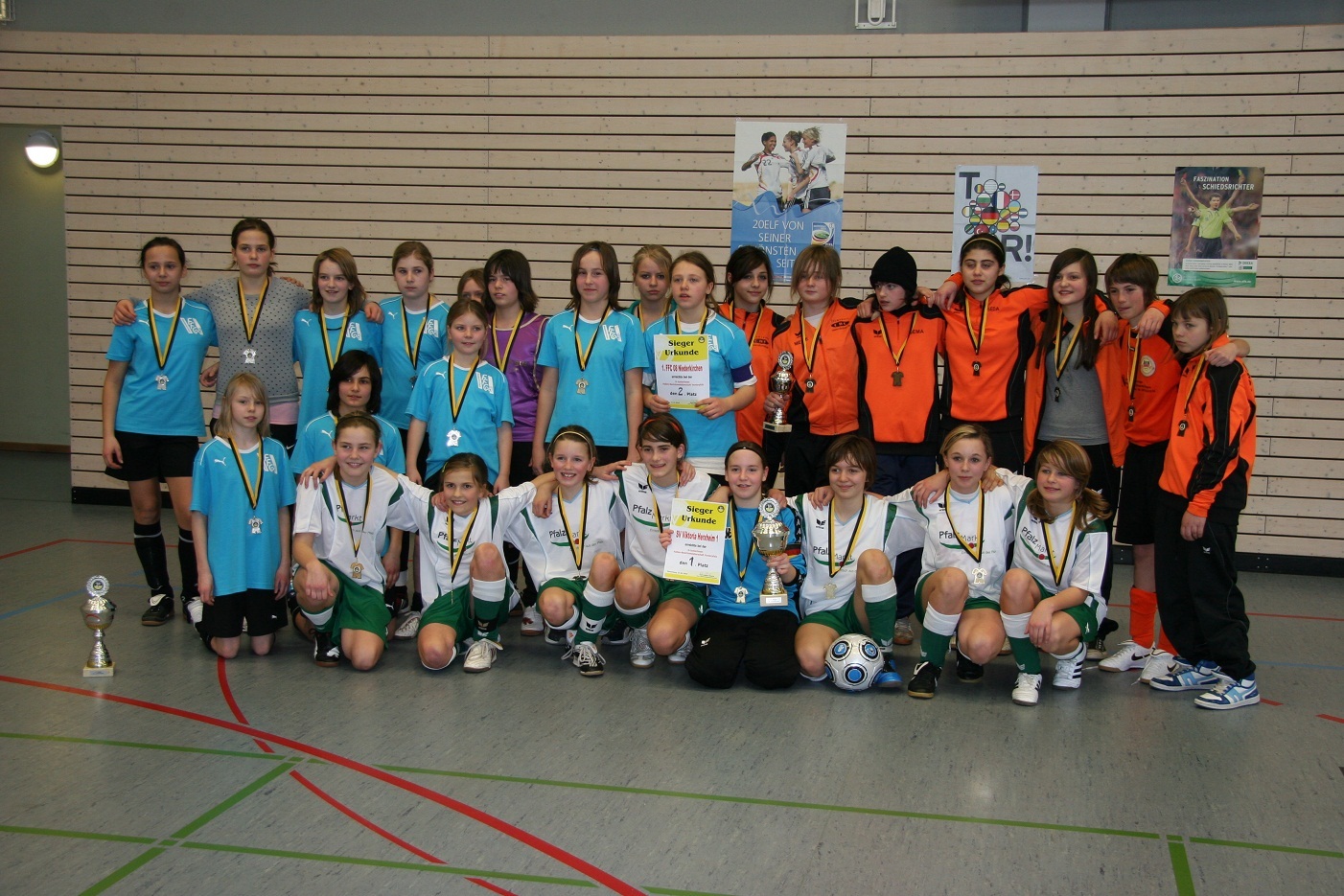 Gruppe junger Fu&szlig;ballspielerinnen in Trikots, die mit Medaillen, Pokalen und Urkunden posieren.
