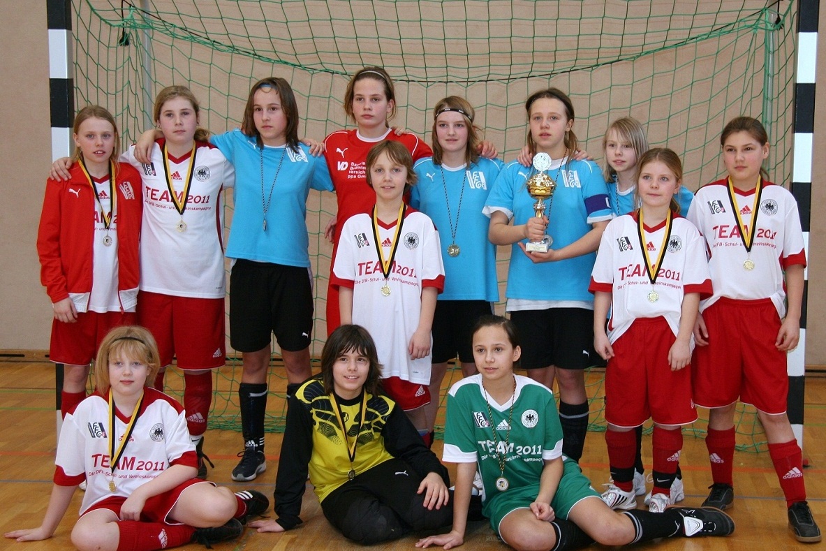 Mannschaftsfoto einer Jugendfu&szlig;ballmannschaft mit Pokal, Medaillen und Netz im Hintergrund.