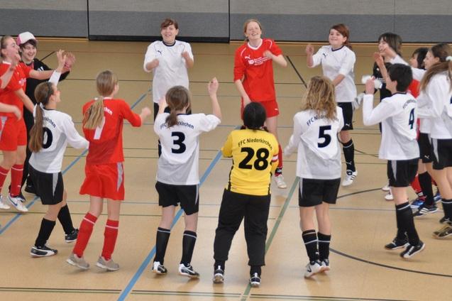 Gruppenspiele mit M&auml;dchenfu&szlig;ballmannschaften in der Halle, die fr&ouml;hlich im Kreis stehen und tanzen.