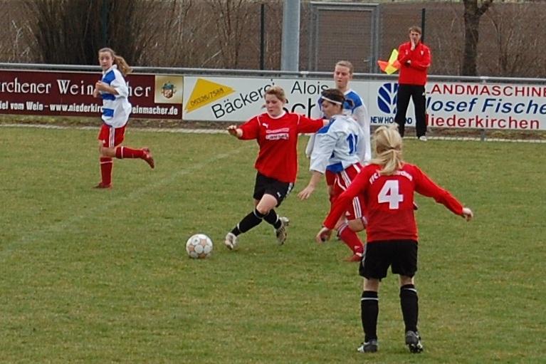 Mädchenfußballspiel auf einem grünen Platz, mehrere Spielerinnen in roten und blauen Trikots, Ball im Spiel.
