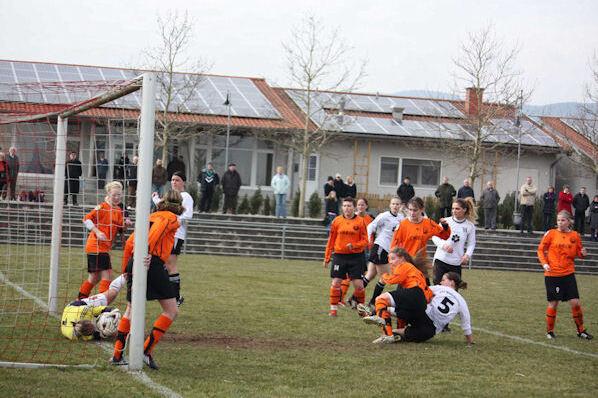 Mannschaft im Fu&szlig;ballspiel: Spielerinnen in orange und schwarz um einen Torraum versammelt, Torwart am Boden.