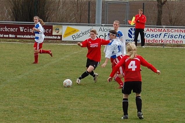 M&auml;dchenfu&szlig;ballspiel auf einem gr&uuml;nen Platz, mehrere Spielerinnen in roten und blauen Trikots, Ball im Spiel.
