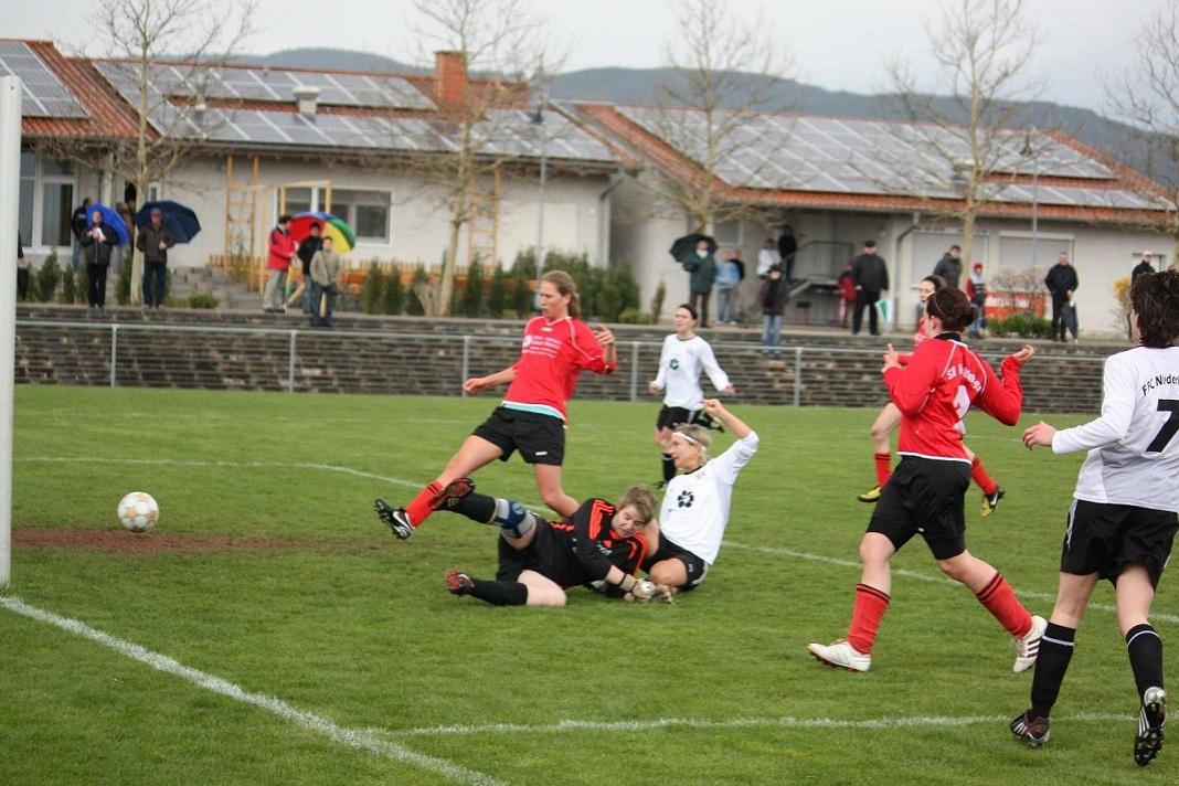 Spielszene im Fu&szlig;ball mit mehreren Spielern in Aktion, ein Torwart im Fallen und ein Ball, der auf das Tor zusteuert.