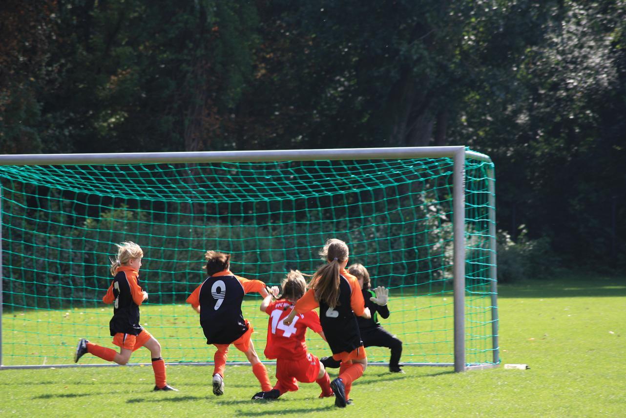 M&auml;dchenfu&szlig;ballmannschaft im Spiel, Torwart und Spielerinnen vor einem Tor auf einem gr&uuml;nen Rasenfeld.