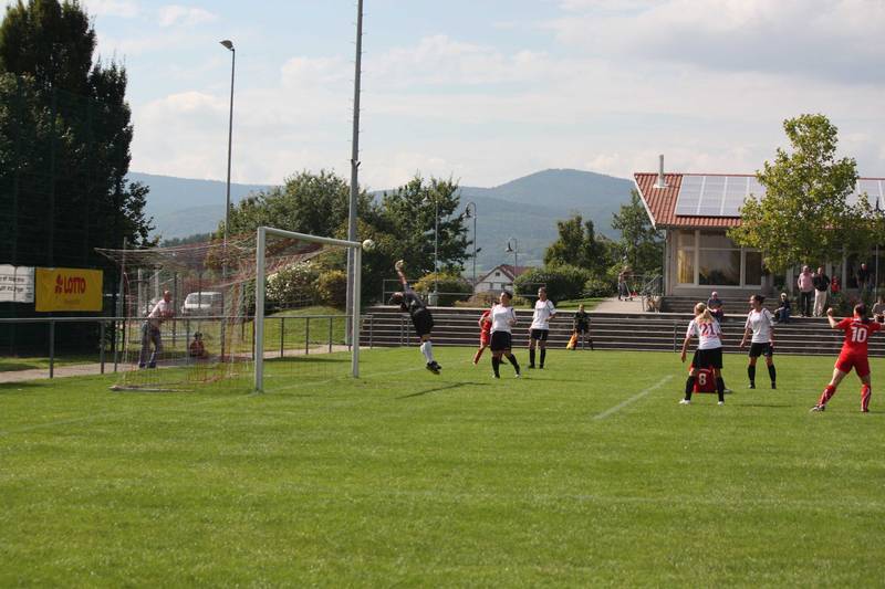 Torwart springt, um den Ball w&auml;hrend eines Fu&szlig;ballspiels zu fangen; Spieler in rot und wei&szlig; stehen auf dem Spielfeld.