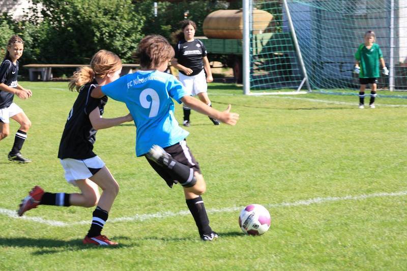 Zwei Kinder spielen Fu&szlig;ball auf einem Rasenplatz; eines dribbelt den Ball, w&auml;hrend das andere es zu stoppen versucht.