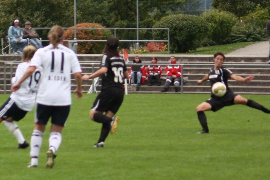 Zwei Spielerinnen im Wettkampf, eine im weißen, die andere im schwarzen Trikot, während der Ball gespielt wird.