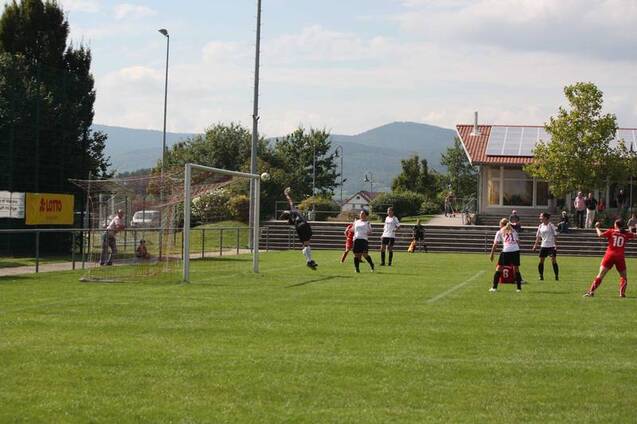 Torwart springt, um den Ball w&auml;hrend eines Fu&szlig;ballspiels zu fangen; Spieler in rot und wei&szlig; stehen auf dem Spielfeld.