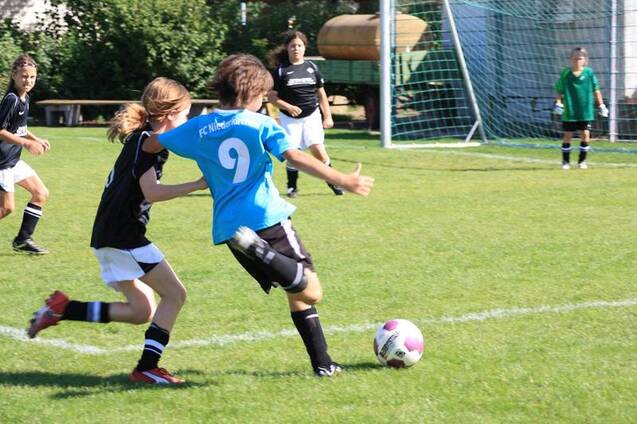 Zwei Kinder spielen Fu&szlig;ball auf einem Rasenplatz; eines dribbelt den Ball, w&auml;hrend das andere es zu stoppen versucht.