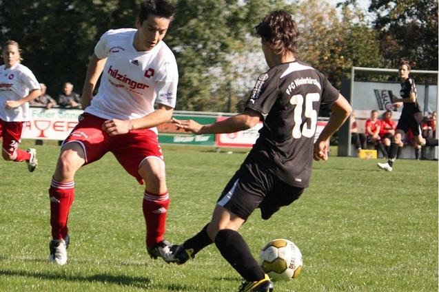 Zwei Fu&szlig;ballspieler im Wettkampf, einer mit wei&szlig;em Trikot und roter Hose, der andere im schwarzen Trikot.