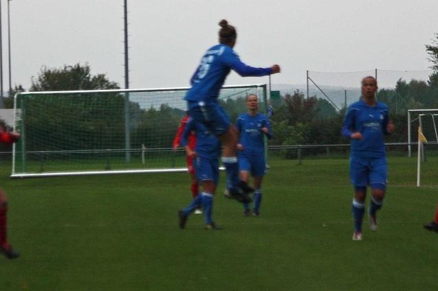 Spielszene eines Frauenteams in blauen Trikots, das ein Tor feiert, w&auml;hrend die Spielerinnen in roten Trikots reagieren.