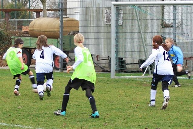 M&auml;dchenfu&szlig;ballspiel: Drei Spielerinnen in gr&uuml;nen Westen laufen auf ein Tor zu, w&auml;hrend die Torh&uuml;terin bereit ist.