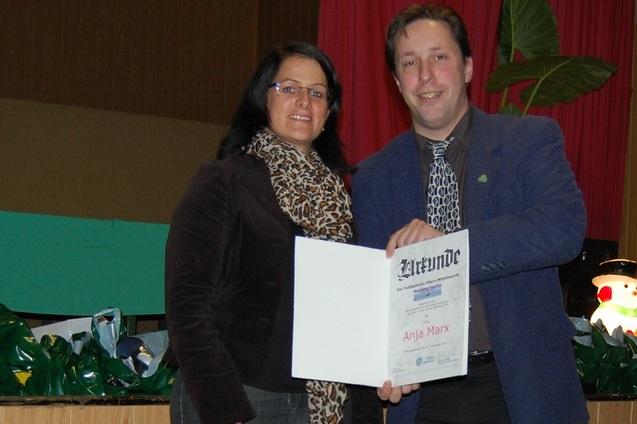 Frau und Mann stehen auf einer B&uuml;hne und halten gemeinsam ein Zertifikat mit dem Namen "Anja Marx" in der Hand.