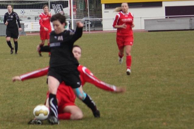Zwei Fu&szlig;ballspielerinnen k&auml;mpfen um den Ball, w&auml;hrend eine Spielerin im roten Trikot zu Boden geht.