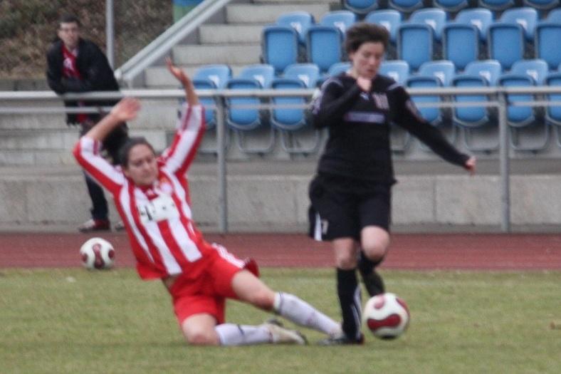 Zwei Frauenspielerinnen im Fußball, eine fällt im roten Trikot, während die andere im schwarzen Trikot vorbeiläuft.