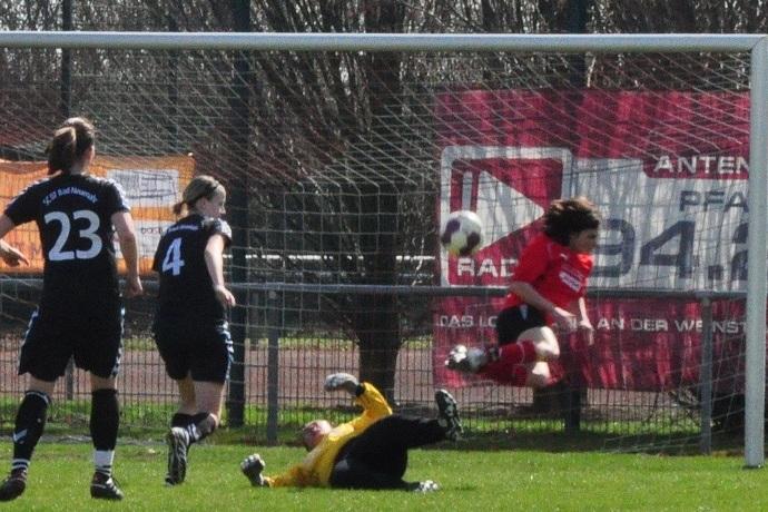 Spielszene im Frauenfu&szlig;ball: Eine Spielerin in rot schie&szlig;t ein Tor, w&auml;hrend die Torh&uuml;terin in gelb zu Boden geht.