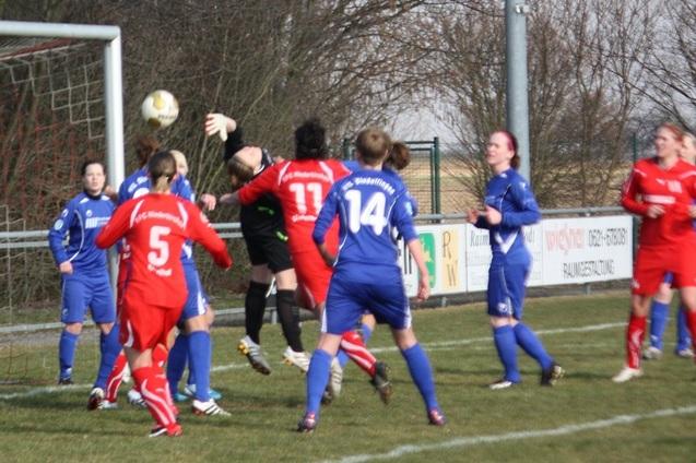 Fu&szlig;ballspiel: Torwart springt nach dem Ball, Spielerinnen in roten und blauen Trikots stehen um den Strafraum herum.