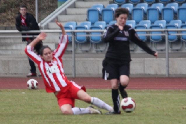 Zwei Frauenspielerinnen im Fu&szlig;ball, eine f&auml;llt im roten Trikot, w&auml;hrend die andere im schwarzen Trikot vorbeil&auml;uft.