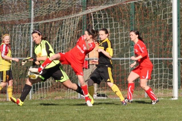 Fu&szlig;ballspiel der Frauen: Spielerin in rotem Trikot wird von der Torh&uuml;terin in gelbem Trikot angegriffen.