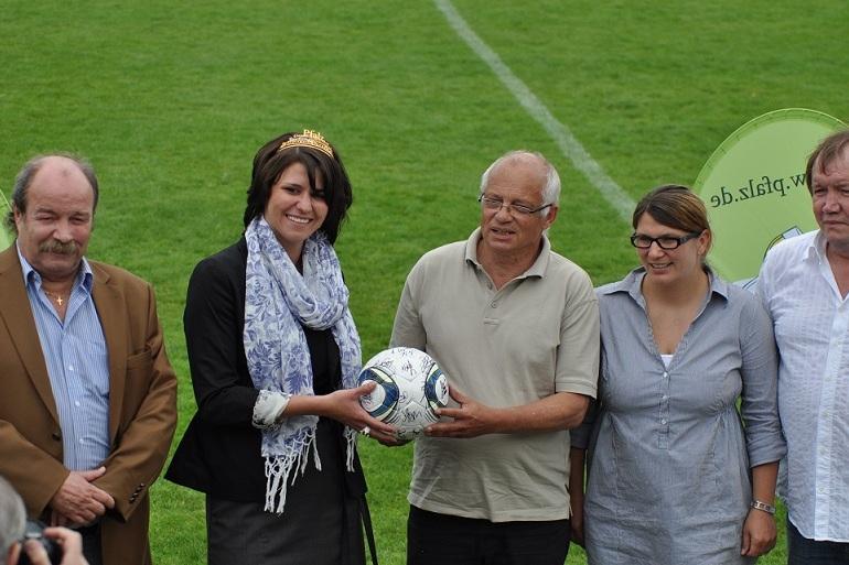 Gruppenshot von vier Personen auf einem Fu&szlig;ballfeld, eine Person h&auml;lt einen Fu&szlig;ball, w&auml;hrend die anderen l&auml;cheln.