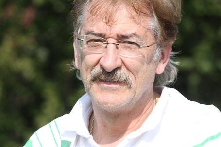 Portr&auml;t eines Mannes mit Brille und Schnurrbart, der in sportlicher Kleidung im Freien steht, mit unscharfem Hintergrund.