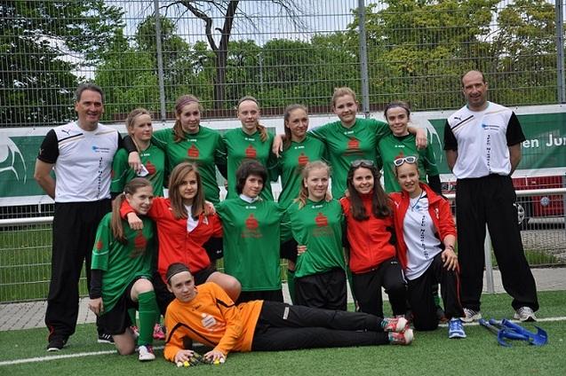 Gruppenshot eines Fu&szlig;ballteams mit M&auml;dchen in gr&uuml;nen Trikots und Trainer in schwarzer und wei&szlig;er Sportbekleidung.