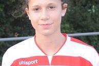 Porträt eines Mädchens in einem weißen Fußballtrikot mit roten Akzenten, lächelnd vor einer grünen Hintergrundkulisse.