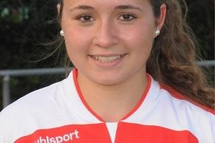 Porträt einer Smiling-Fußballspielerin im weißen Trikot mit roten Akzenten, Hintergrund mit verschwommenem Fußballfeld.