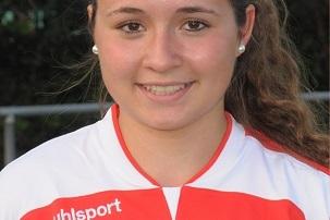 Portr&auml;t einer Smiling-Fu&szlig;ballspielerin im wei&szlig;en Trikot mit roten Akzenten, Hintergrund mit verschwommenem Fu&szlig;ballfeld.