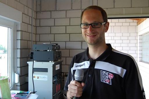 Mann mit Brille h&auml;lt ein Mikrofon in einem Raum mit Technik und Blick nach drau&szlig;en.