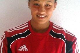 Portr&auml;t einer jungen Frau mit einem Dutt, die in einem roten Adidas-Sportshirt l&auml;chelt und die Arme verschr&auml;nkt.