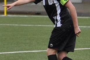 Junger Fu&szlig;ballspieler mit Kapit&auml;nsbinde, der auf einem Kunstrasenfeld in Richtung des Spiels zeigt.