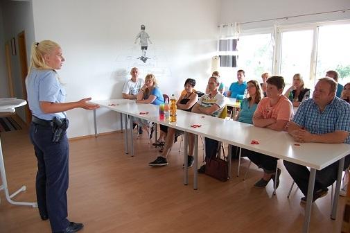 Polizistin spricht vor einer Gruppe von Zuh&ouml;rern in einem hellen Seminarraum. Tische sind mit Getr&auml;nken und Kugeln dekoriert.