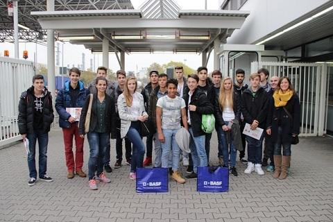 Gruppe von Jugendlichen steht vor einem Eingang mit BASF-Logos, umgeben von grauen Pflastersteinen und Gebäuden.