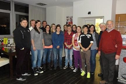 Gruppe von 15 Personen posiert l&auml;chelnd in einem Raum mit modernen M&ouml;beln und beleuchteter K&uuml;che.