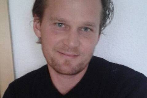 Portr&auml;t eines Mannes mit kurzem, unordentlichem Haar, der in die Kamera l&auml;chelt, vor einem hellen Hintergrund.