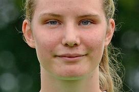 Portr&auml;t einer jungen Sportlerin mit blondem Haar, die ein gr&uuml;nes Trikot tr&auml;gt, vor unscharfem Hintergrund.