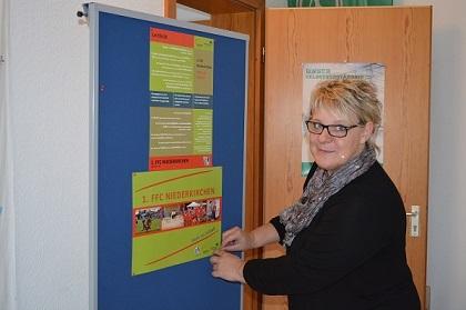 Frau befestigt ein farbige Plakat an einer Pinnwand in einem Raum.