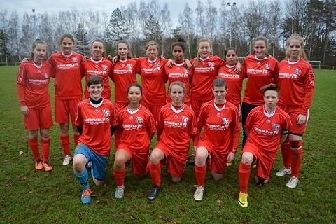 Gruppe von 15 Frauen in roten Fu&szlig;balltrikots auf einem Rasenplatz, l&auml;chelnd und in zwei Reihen aufgestellt.