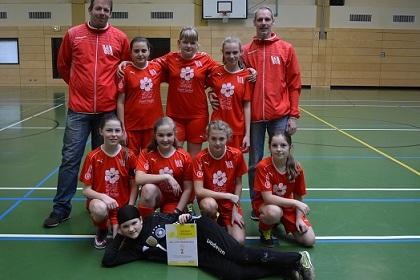 Mädchen-Fußballmannschaft in roten Trikots mit Trainer, Pose auf Sportfeld, Urkunde in der Mitte.