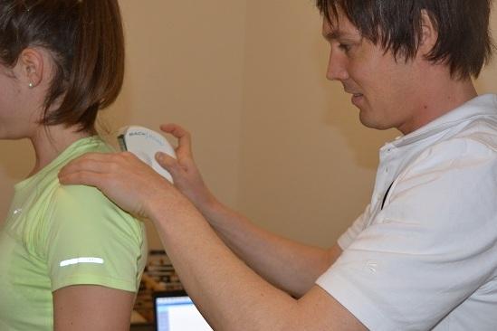 Therapeut f&uuml;hrt eine Behandlung an der Schulter einer Patientin in einem hellen Raum durch.