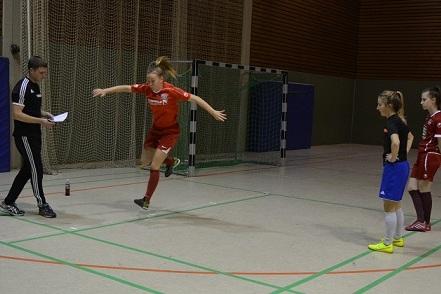 Eine Spielerin in rotem Trikot springt w&auml;hrend des Trainings in einer Sporthalle, w&auml;hrend ein Trainer Anweisungen gibt.