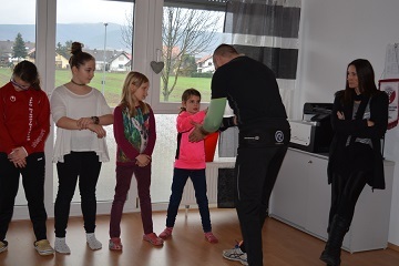 Gruppenschulung mit Kindern, Lehrperson demonstriert eine Technik, Teilnehmer h&ouml;ren aufmerksam zu. R&auml;ume mit Fenstern.