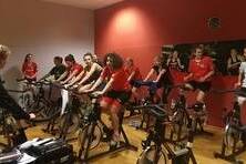 Gruppe von acht Radfahrern in einem Spinning-Kurs, begleitet von einer Trainerin in einem modernen Fitnessstudio.