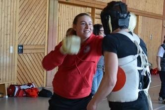 Eine junge Frau schl&auml;gt mit gepolsterten Handschuhen auf einen Mann mit Schutzweste w&auml;hrend des Trainings.