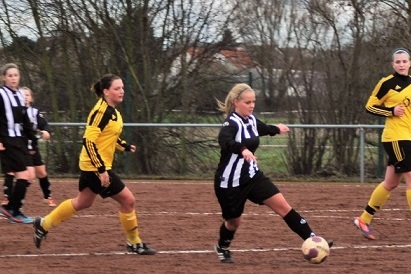 Frauenfu&szlig;ballspiel mit Spielerinnen in schwarz-wei&szlig; gestreiften und gelben Trikots, eine Spielerin tritt den Ball.