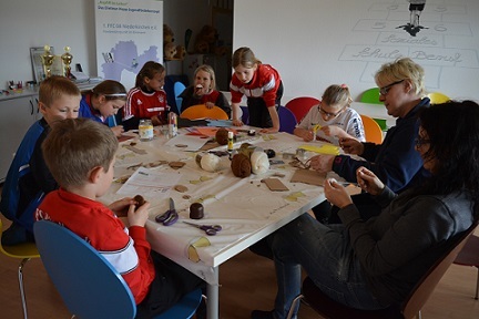 Gruppe von Kindern und Erwachsenen beim Basteln an einem Tisch, umgeben von Bastelmaterialien und Werkzeugen.
